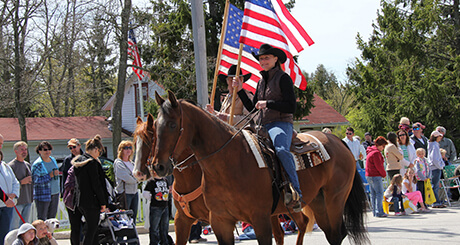 People watching a parade with people on horse-back carrying flags.