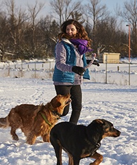 A woman running through the snow with two dogs.