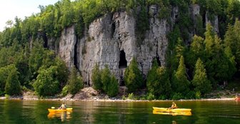Two kayakers in front of tree-lined cliffs