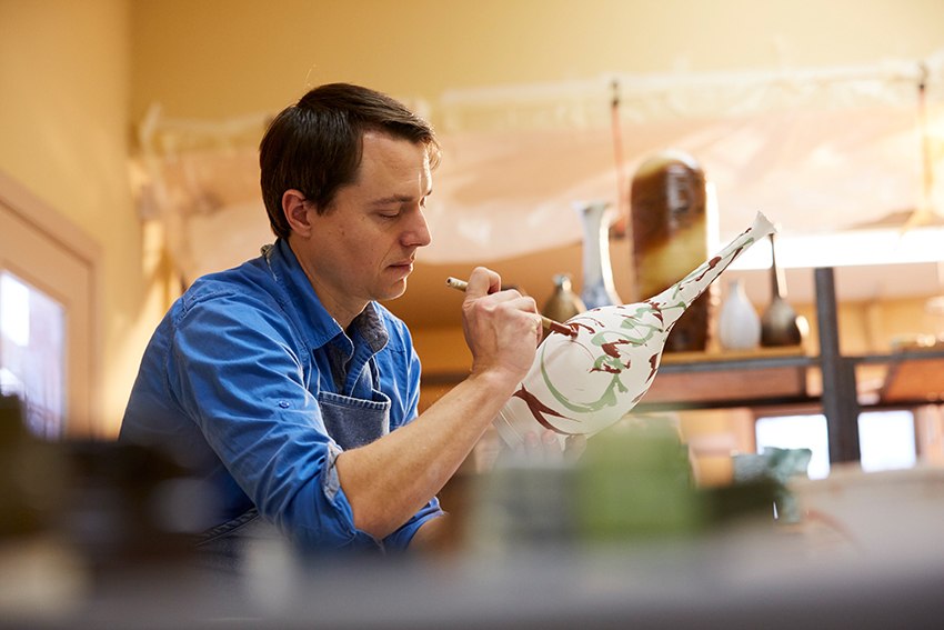 An artist paints a ceramic vase in his studio