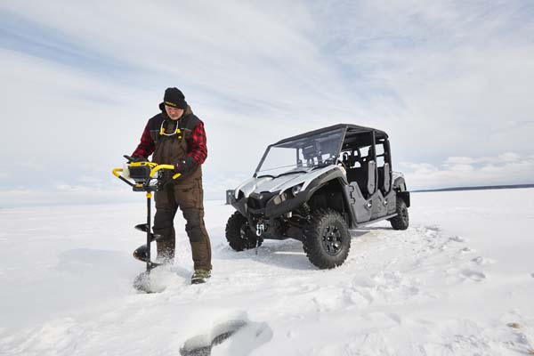 A man drills a hole into the ice with an all-terrain vehicle behind him.