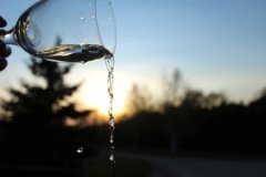 Closeup of a glass pouring liquid with the landscape silhouetted in the background.