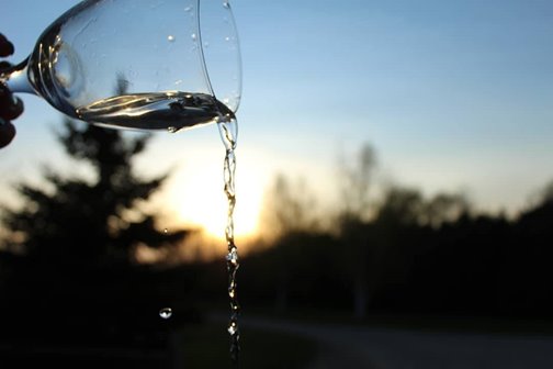 Closeup of a glass pouring liquid with the landscape silhouetted in the background.