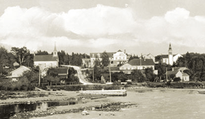 Historical black and white photo of buildings along the shoreline.