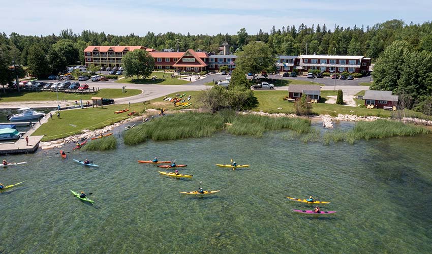 A dozen kayakers practice their skills on Lake Michigan, with Rowleys Bay Resort in the background.