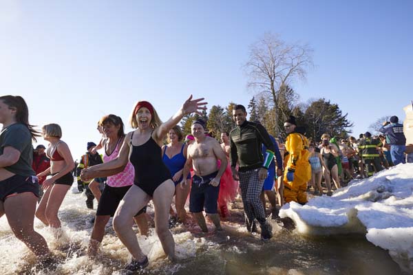 A large crowd is costumes and swimwear runs into the snowy lake.