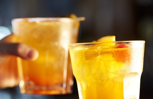 Two old-fashioned cocktails sitting on a bar.