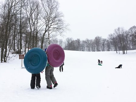 People carrying innertubes up a snowhill