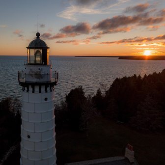 The sun setting in the distance with a white lighthouse in the foreground.