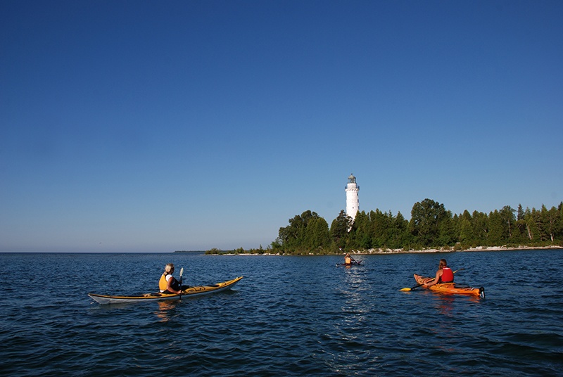 Kayakers paddle towards a lighthouse