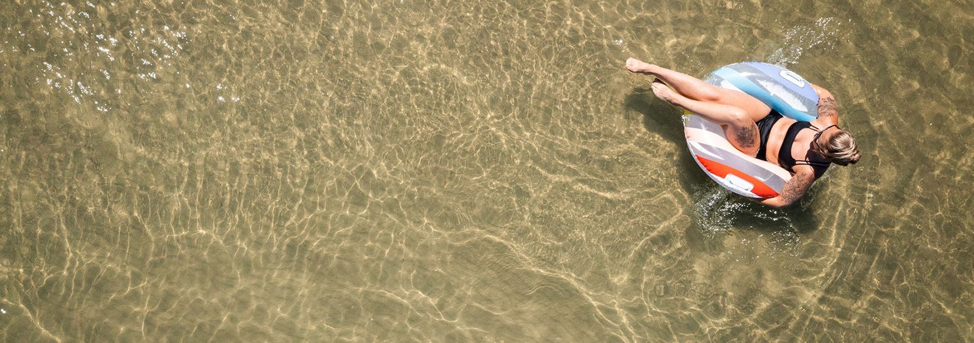 A woman in an innertube in shallow water from above.