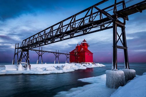 A red lighthouse at the end of a snowy pier.