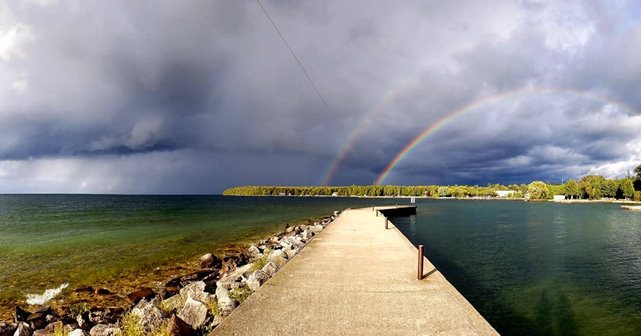 A double rainbow at the end of a pier on a cloudy day.