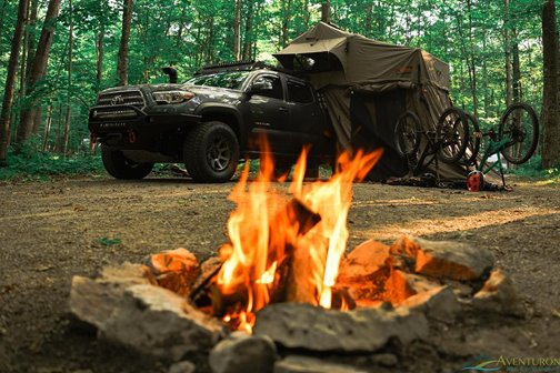 Campfire in the foreground with a pickup truck and pop-up tent attached in the background
