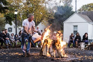 A man pours fuel on an outdoor fire in front of a crowd at a fish boil