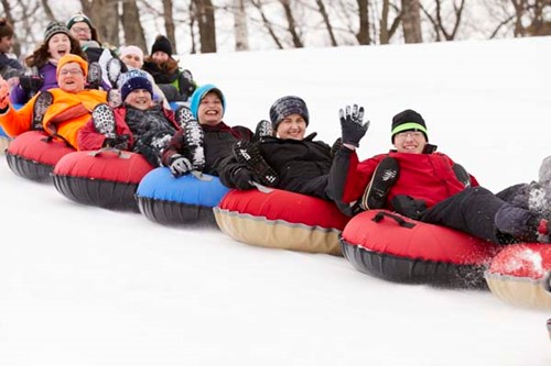 Smiling kids sledding down a hill in a line.