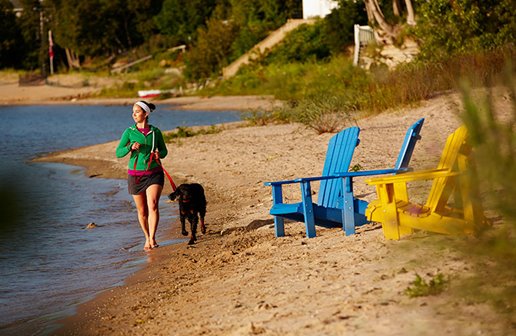 A woman jogging on the beach with a dog.