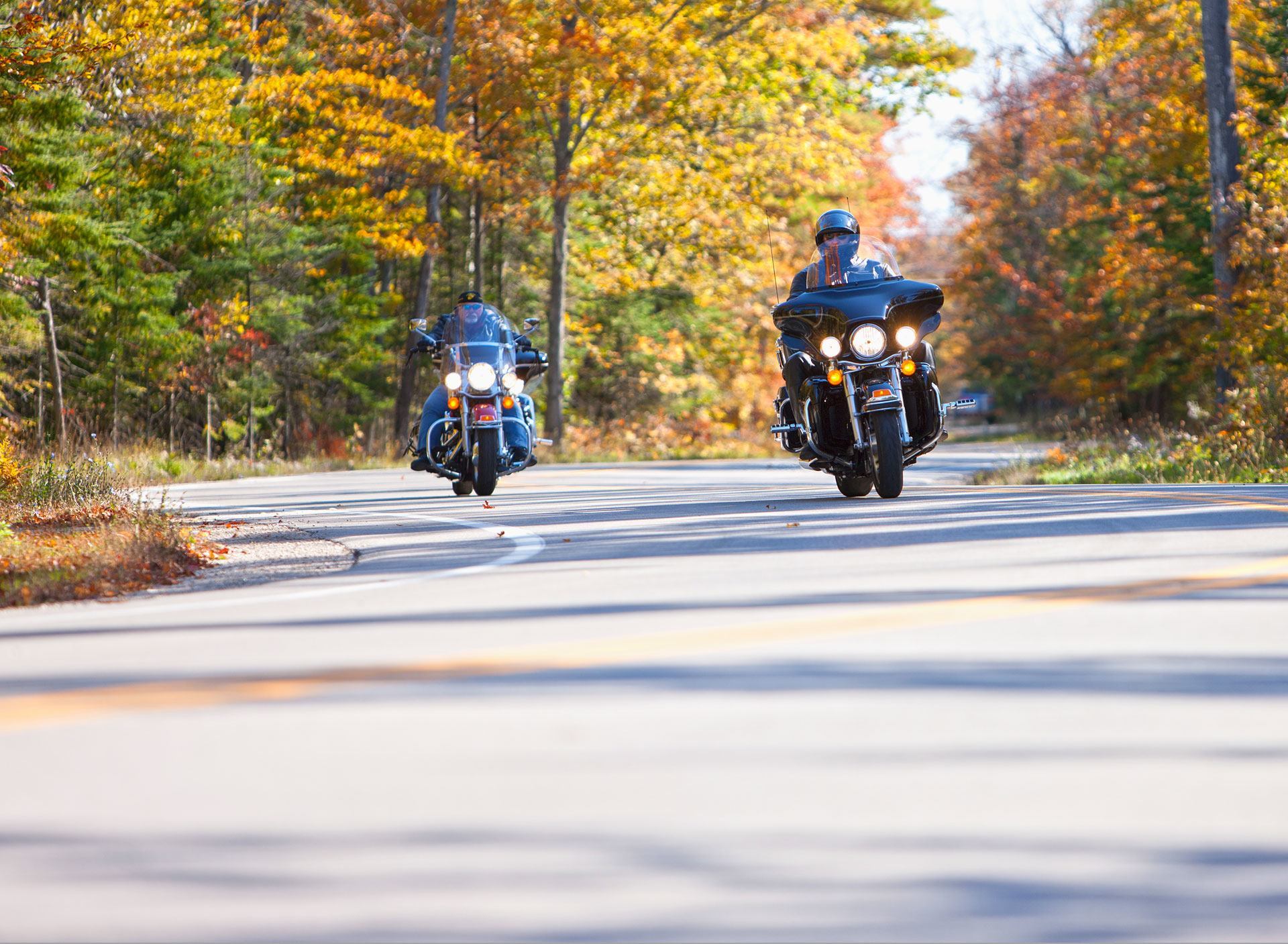 Two motorcyclists driving down a road through the woods.