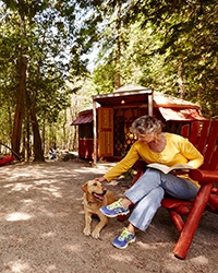 A woman sitting at a campsite petting a dog.