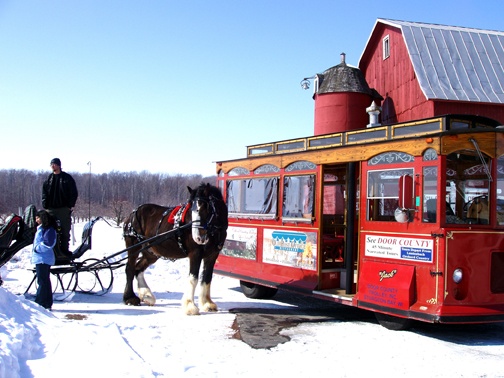 A horse and carriage next to a trolley car in the snow