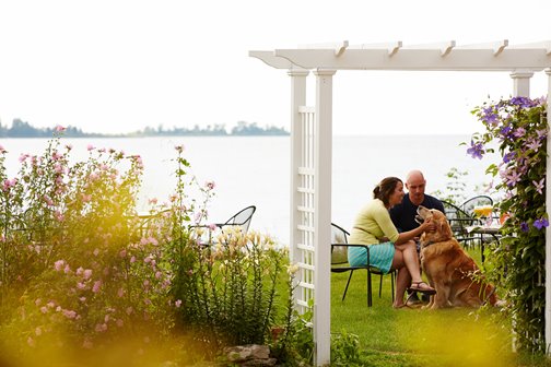 A couple with a dog at the lakefront behind a gazebo.
