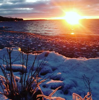 The sun rising over the snowy shore of the lake.