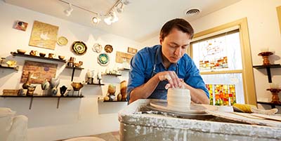 Person spinning clay on a pottery wheel in a pottery studio.