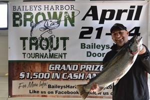 Man holding up a large fish in front of a trout contest sign.