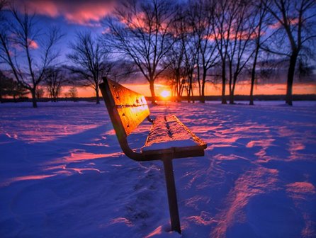 A bench in the snow at sunset.