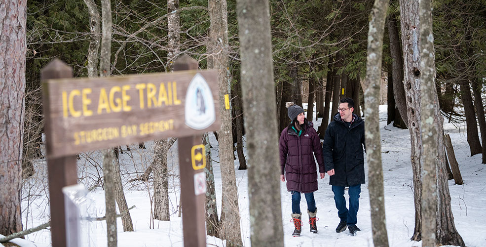 A couple in the snow walking toward an Ice Age Trail sign.