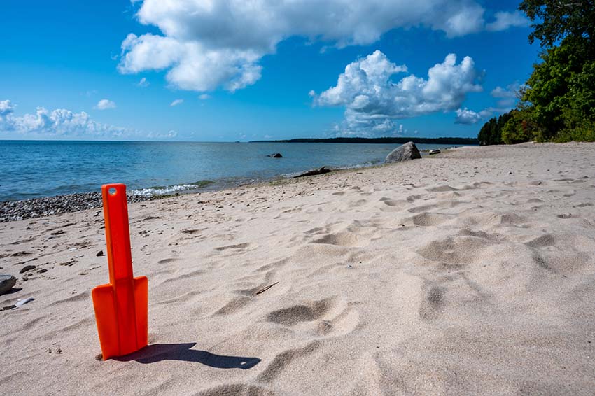 A bright red shovel standing upright in the sand on a remote beach.