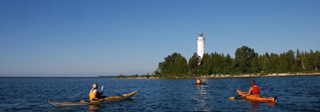 Three kayakers offshore in front of a lighthouse.