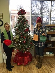 Two women holding winter hats next to a Christmas tree.