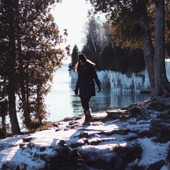 A woman walking along a snowy bank at the lakefront.