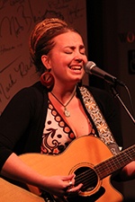 A woman singing and playing acoustic guitar.