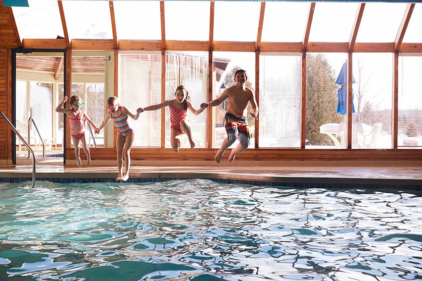 Kids jumping into an indoor pool with snow and ice outside.
