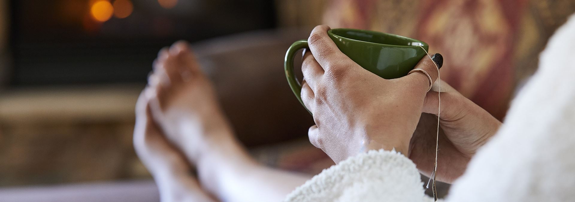 A person wearing a white robe with their feet up holding a cup of tea.
