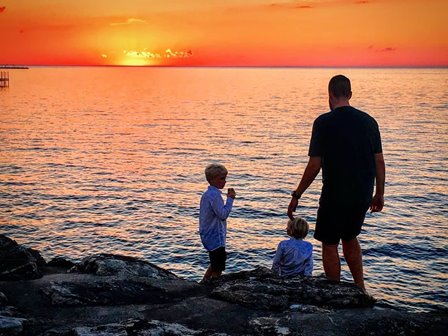 A man with two children watching the sunset at the lakefront.