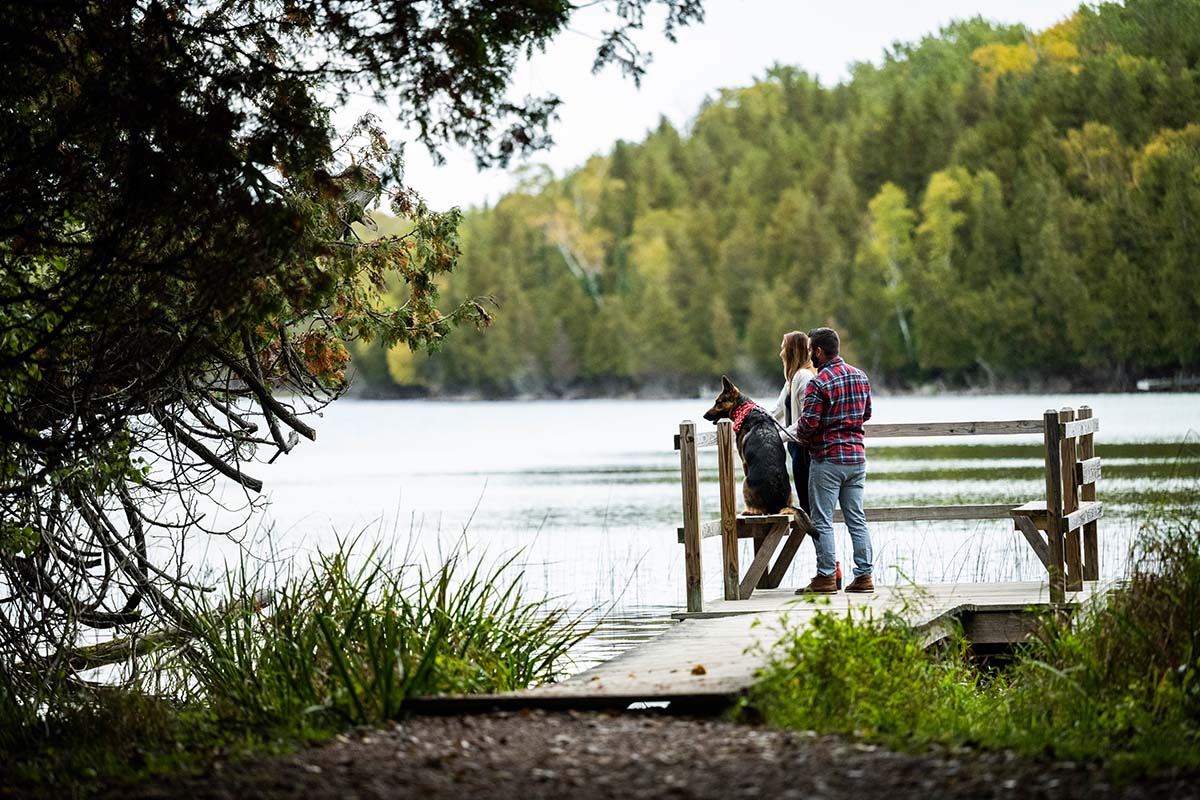 A couple and their dog looks out at Little Lake from a peaceful dock.