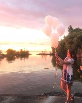 A woman holding white balloons at the lakefront.
