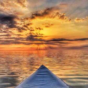 The tip of a kayak looking out at the sunset over the lake.