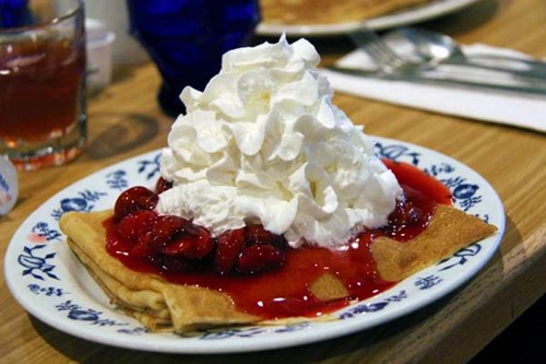 A plate of Swedish pancakes smothered in cherry sauce and whipped cream.