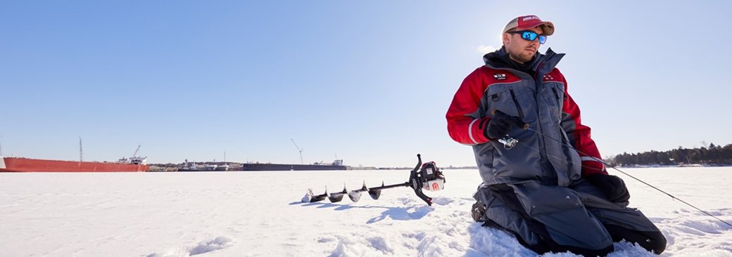 A person kneeling in the snow ice fishing.