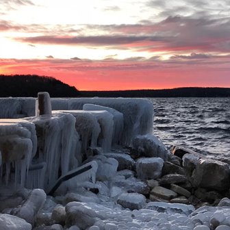 A pink sunset beyond the ice-covered rocks of the lakefront.