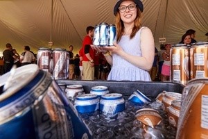 Woman holding up cans of beer in front of a beer cooler.