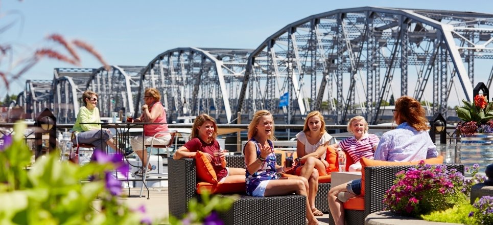 Women sitting on an outdoor patio in front of a metal bridge.