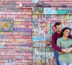 Man with his arms around a woman leaning up against a graffiti covered wall.