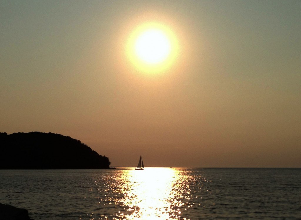 The sun setting over a sailboat on the lake.
