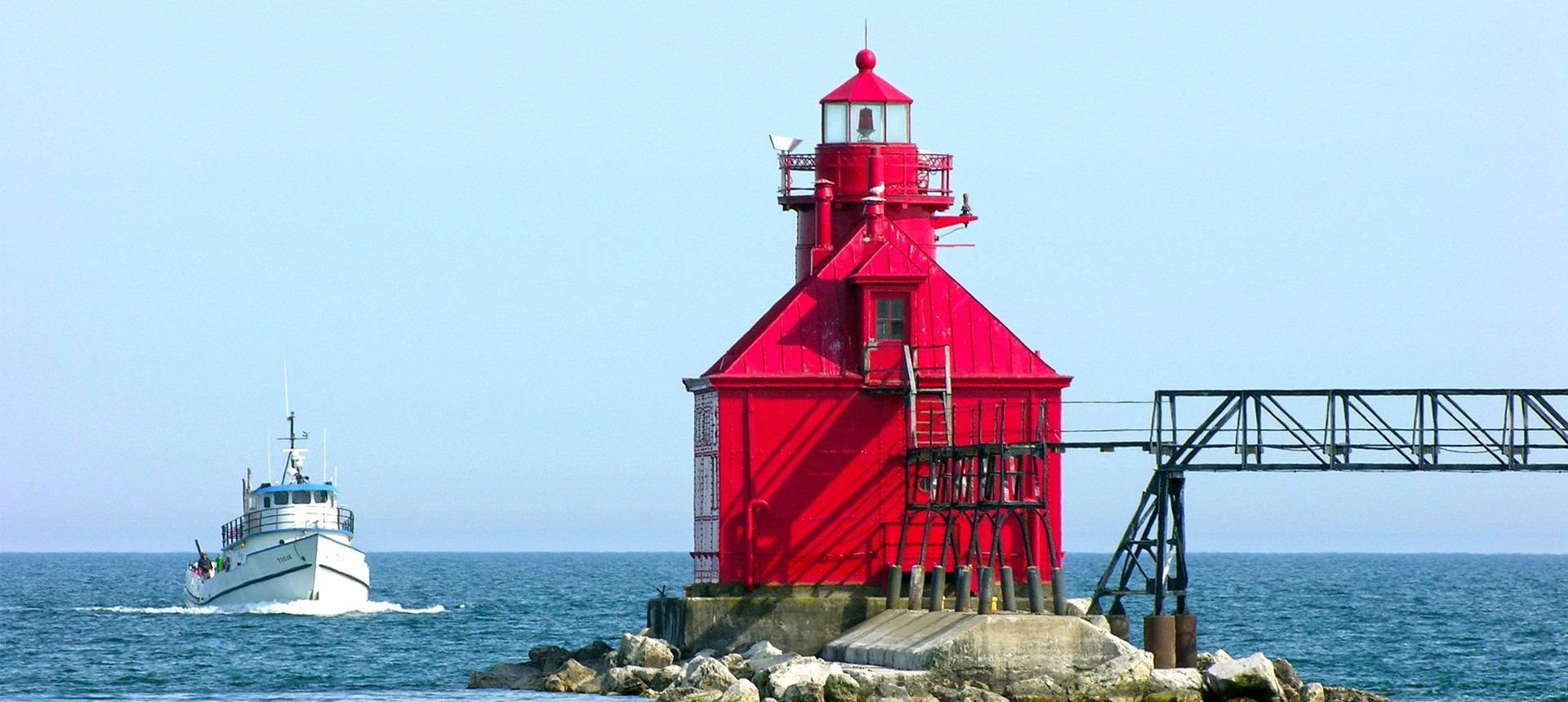Red lighthouse on a rocky outcropping with a boat coming in