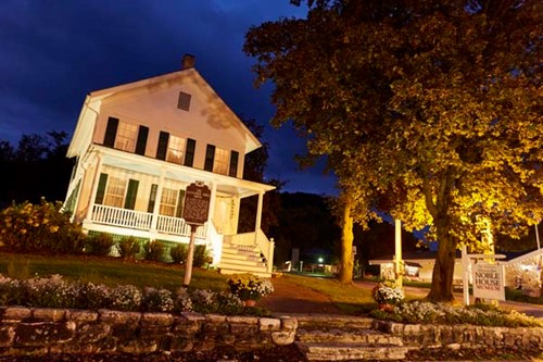 The Alexander Noble house, in Greek-revival style, illuminated at night.
